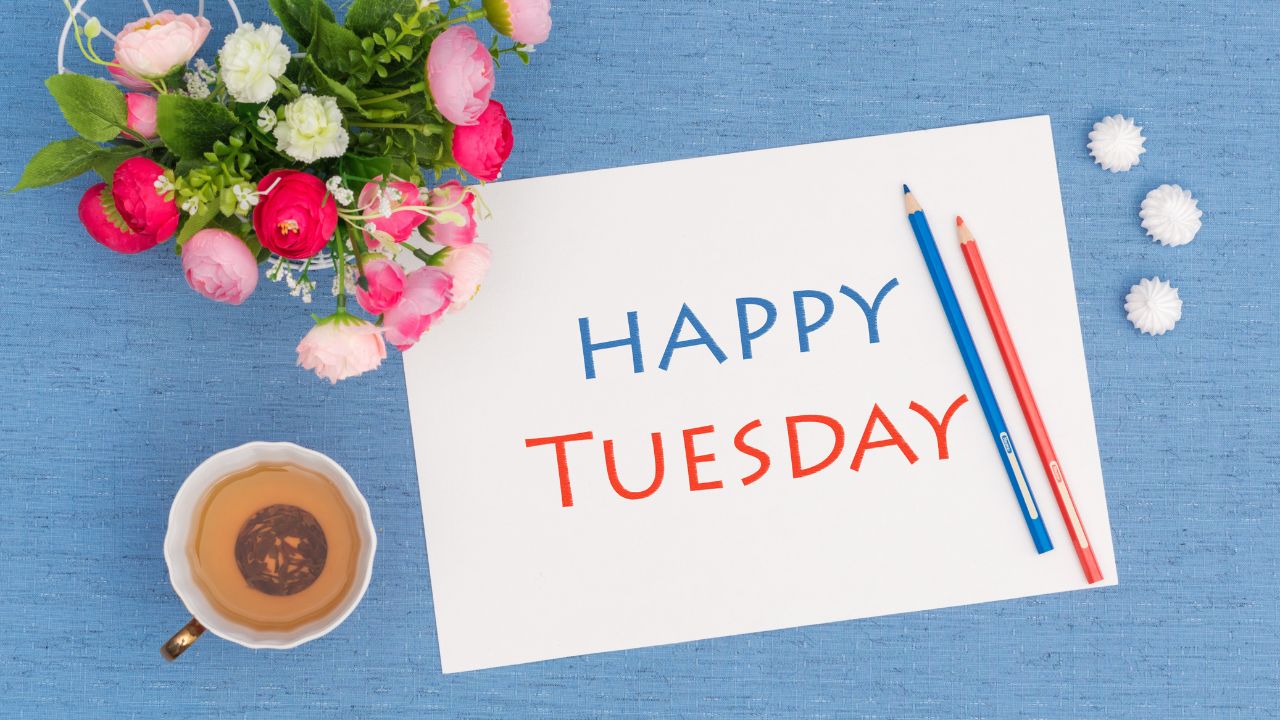 A cheerful setup featuring a "Tuesday Morning Prayer" note, a bouquet of fresh flowers, two colored pencils, and a cup of tea on a blue background.