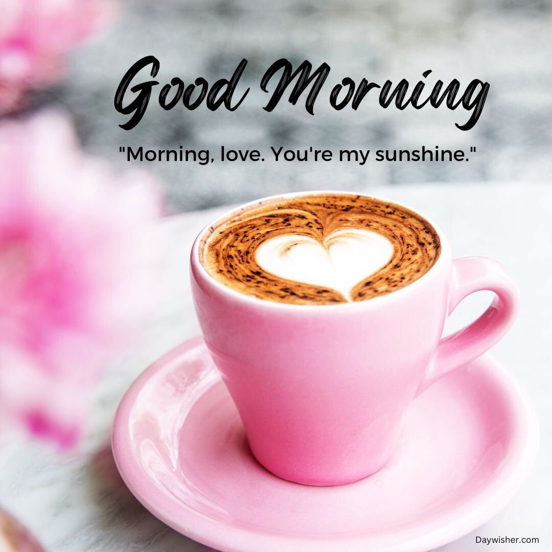 A pink coffee cup with a heart-shaped foam design on a marble surface, accompanied by pink flowers and the text "Good Morning Love" and "Morning, love. You're my sunshine.