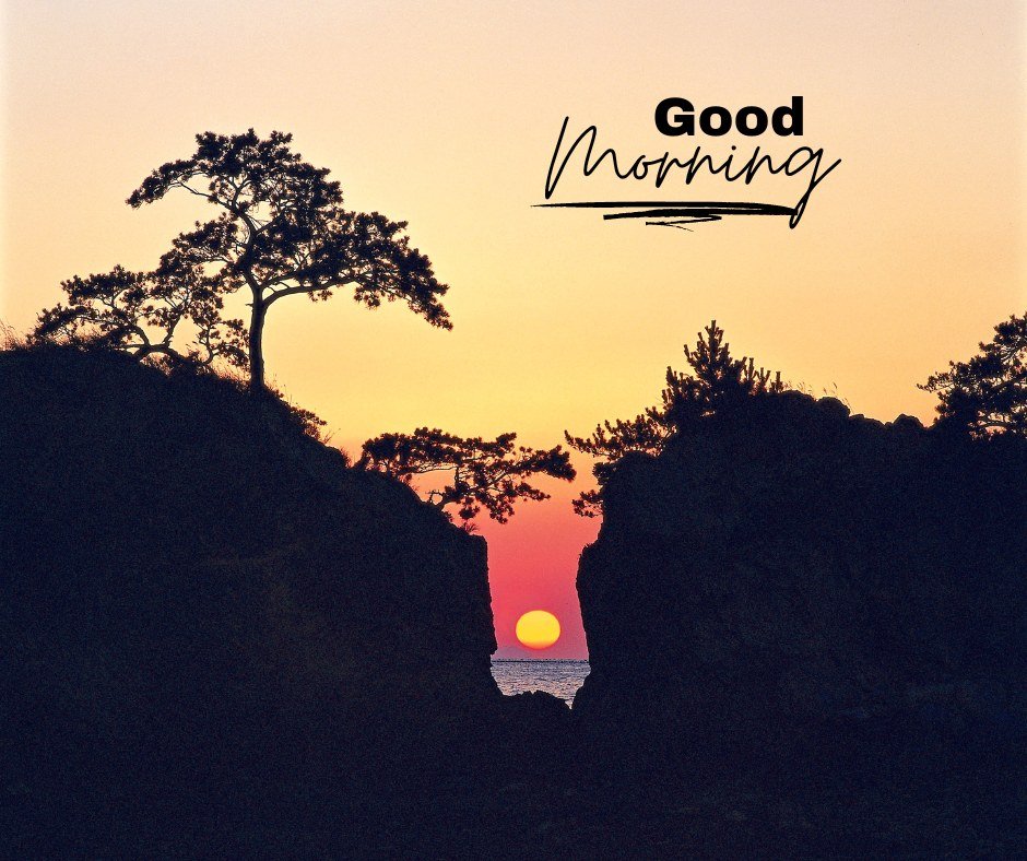 A serene sunrise viewed through a gap between rocky cliffs, with silhouetted trees and the text "Good Morning." The sky displays a gradient of warm colors from orange to pink. This image captures the tranquility of a natural landscape at dawn, ideal for good morning nature images, beautiful good morning nature images, and sunrise good morning nature images.