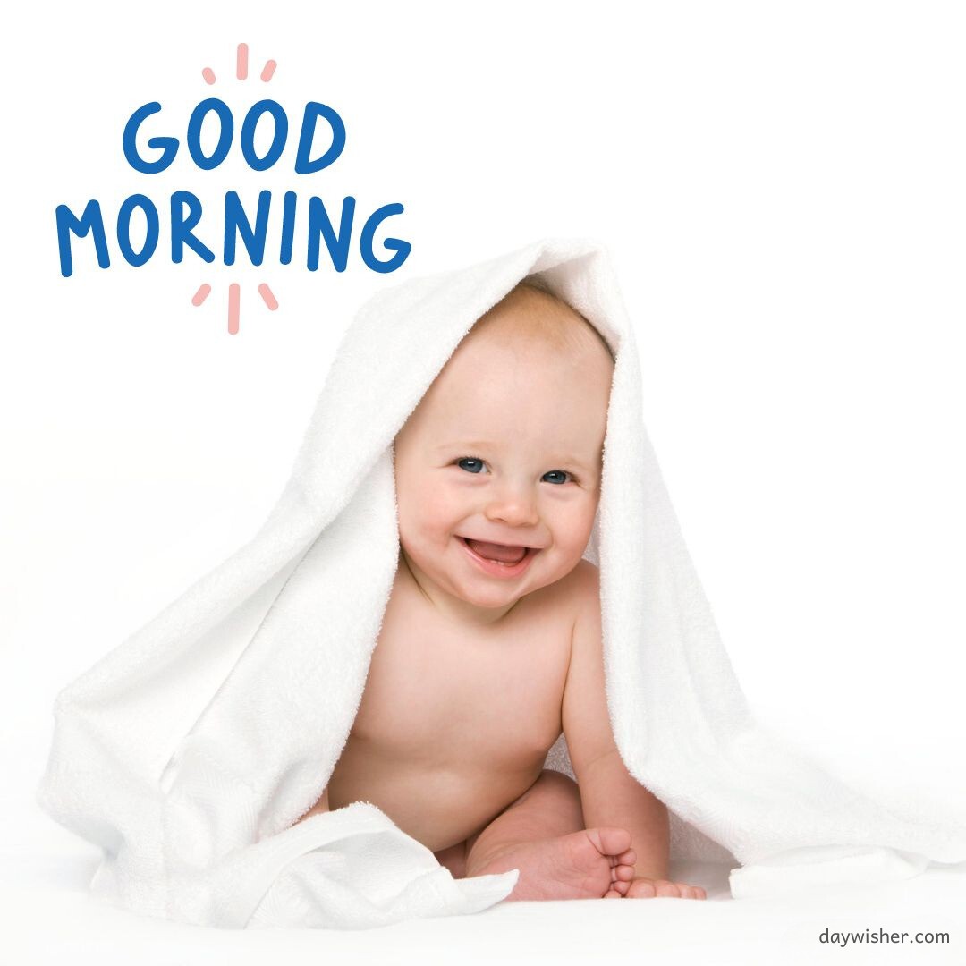 A cheerful baby under a white towel, beaming with a delightful smile, accompanied by a "Good Morning" message in playful blue letters, perfect for a good morning baby image post