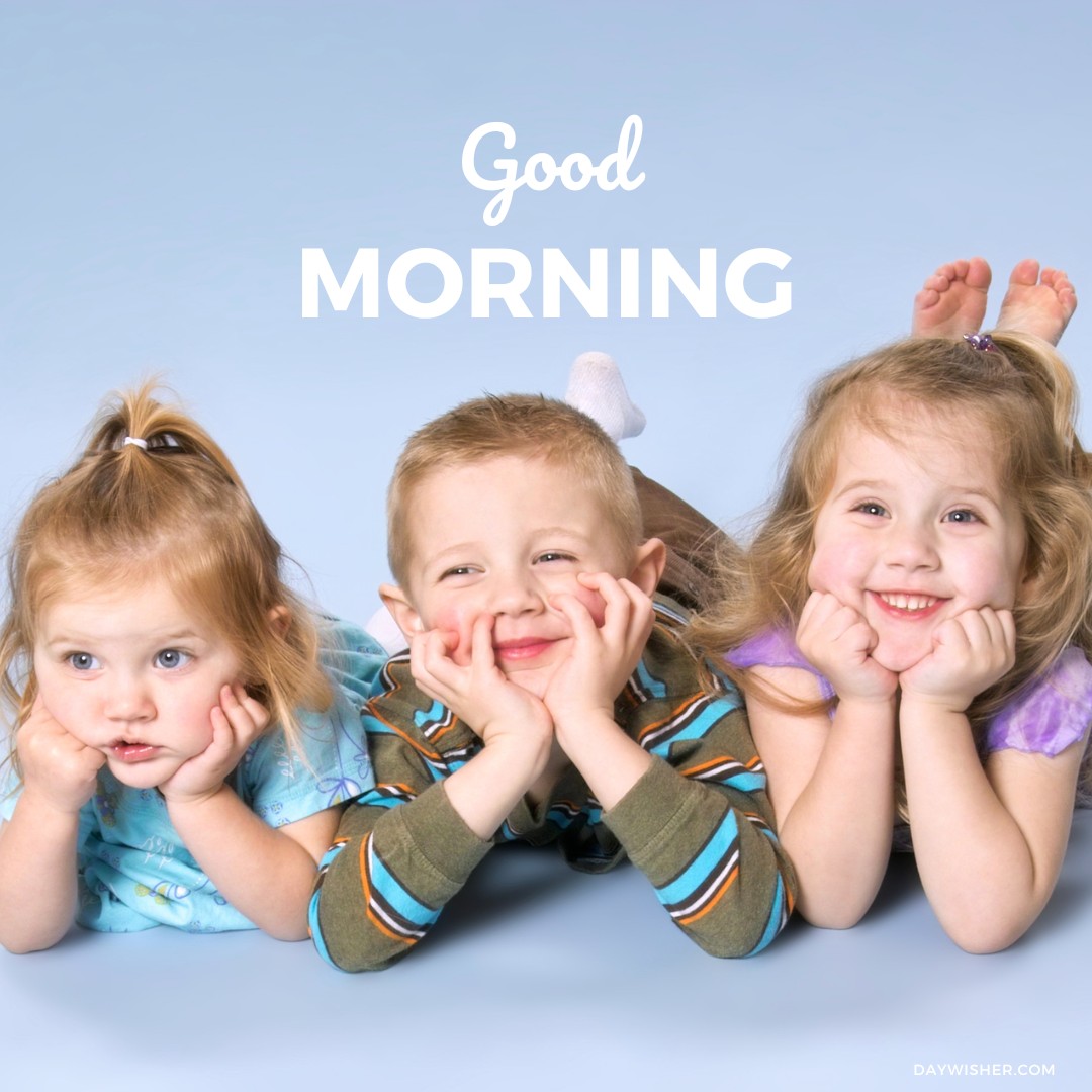 Three joyful children lying on their stomachs, smiling at the camera with playful expressions, two girls and one boy, enhancing a cheerful good morning baby greeting