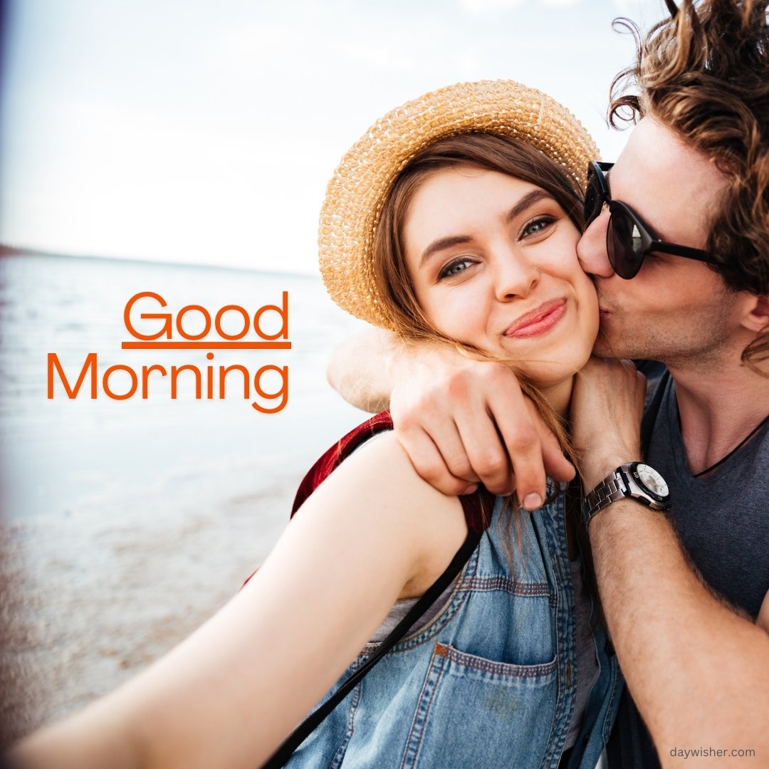 A couple taking a selfie at the beach. The man is wearing sunglasses and a watch, kissing the smiling woman on the cheek, who is wearing a straw hat and denim jacket. The text "Good Morning" is written in orange on the left side of the image.