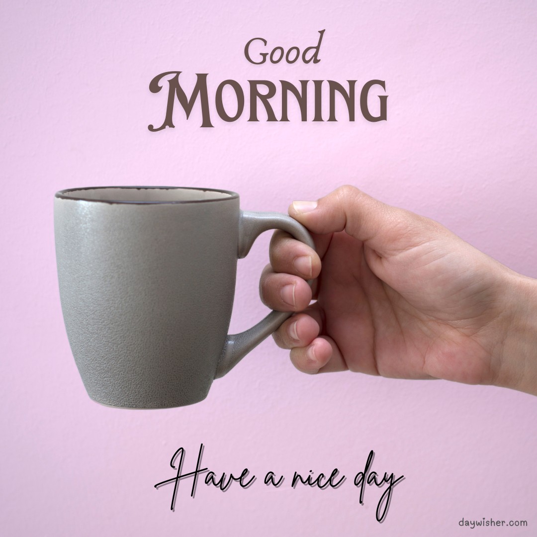 A hand holding a stylish matte grey coffee mug against a soft pink background with 'Good Morning' and 'Have a nice day' texts—perfect for a calm and inspiring morning greeting.