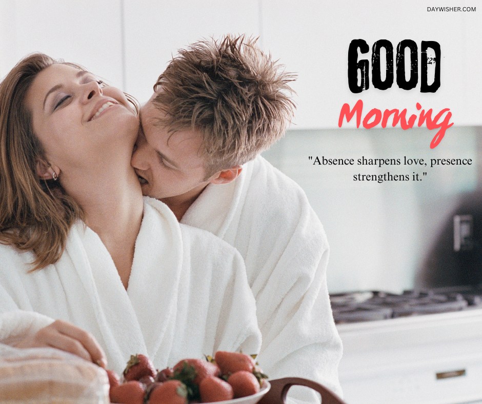 A couple sharing an intimate moment in the kitchen. Both are wearing white bathrobes, with the man kissing the woman's neck from behind. The woman smiles with her eyes closed, holding a bowl of strawberries. The text "Good Morning" is written in bold black and red script, along with the quote, "Absence sharpens love, presence strengthens it."