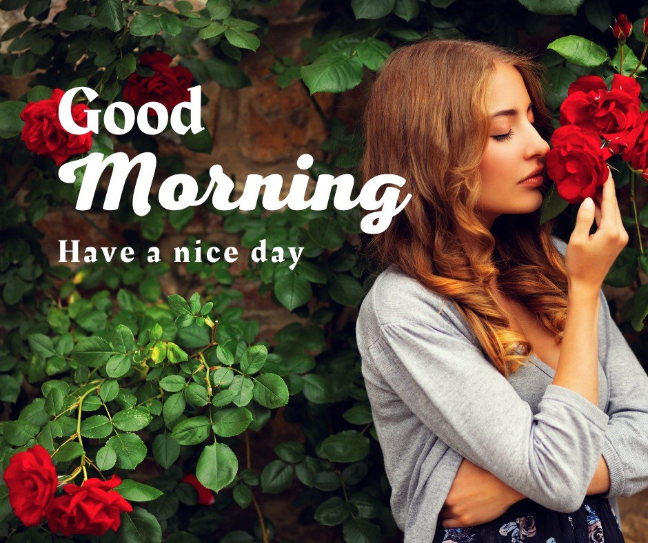 A serene image of a woman gently smelling a vibrant red rose in a lush garden setting, with "Good Morning - Have a nice day" elegantly scripted across the top. This captivating scene combines the freshness of nature with a moment of peaceful reflection, perfectly suited for a rejuvenating and inspiring morning greeting.