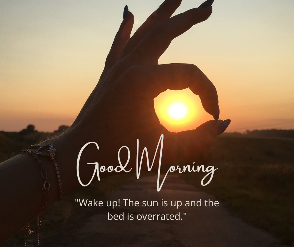 A hand forming a circle with fingers, framing the rising sun in the background, casting a warm glow over the landscape. The text "Good Morning" is displayed along with the humorous quote "Wake up! The sun is up and the bed is overrated." This image captures the essence of a beautiful good morning with natural sunshine, perfect for sharing positivity and a touch of humor.