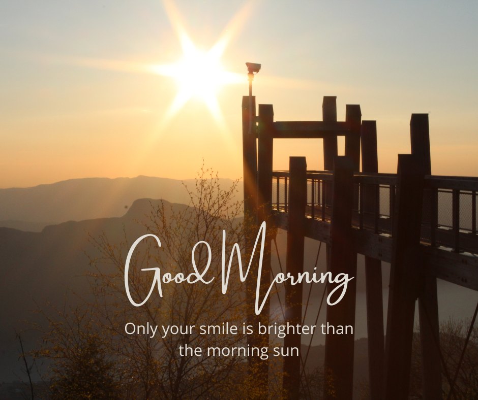 A beautiful sunrise with the sun's rays shining brightly over a scenic viewpoint, casting a warm glow on the landscape. The text "Good Morning" is displayed along with the quote "Only your smile is brighter than the morning sun." This image captures the essence of a beautiful good morning with natural sunshine, perfect for sharing positivity and inspiration.