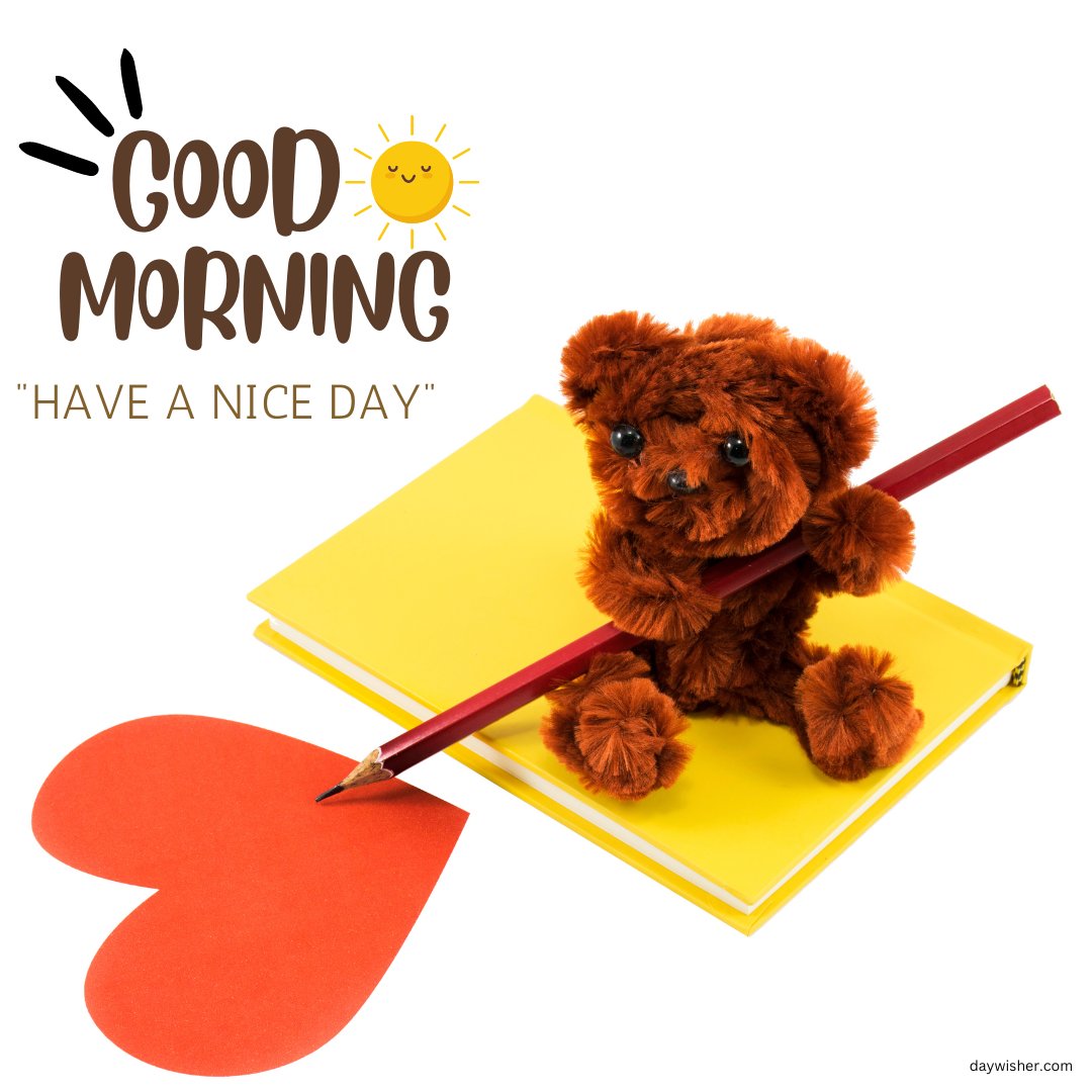 A small good morning teddy bear holding a pencil, sitting on a yellow notebook, and drawing a red heart. The image features the text "Good Morning - Have a Nice Day" with a cheerful sun illustration, creating a positive and creative vibe.