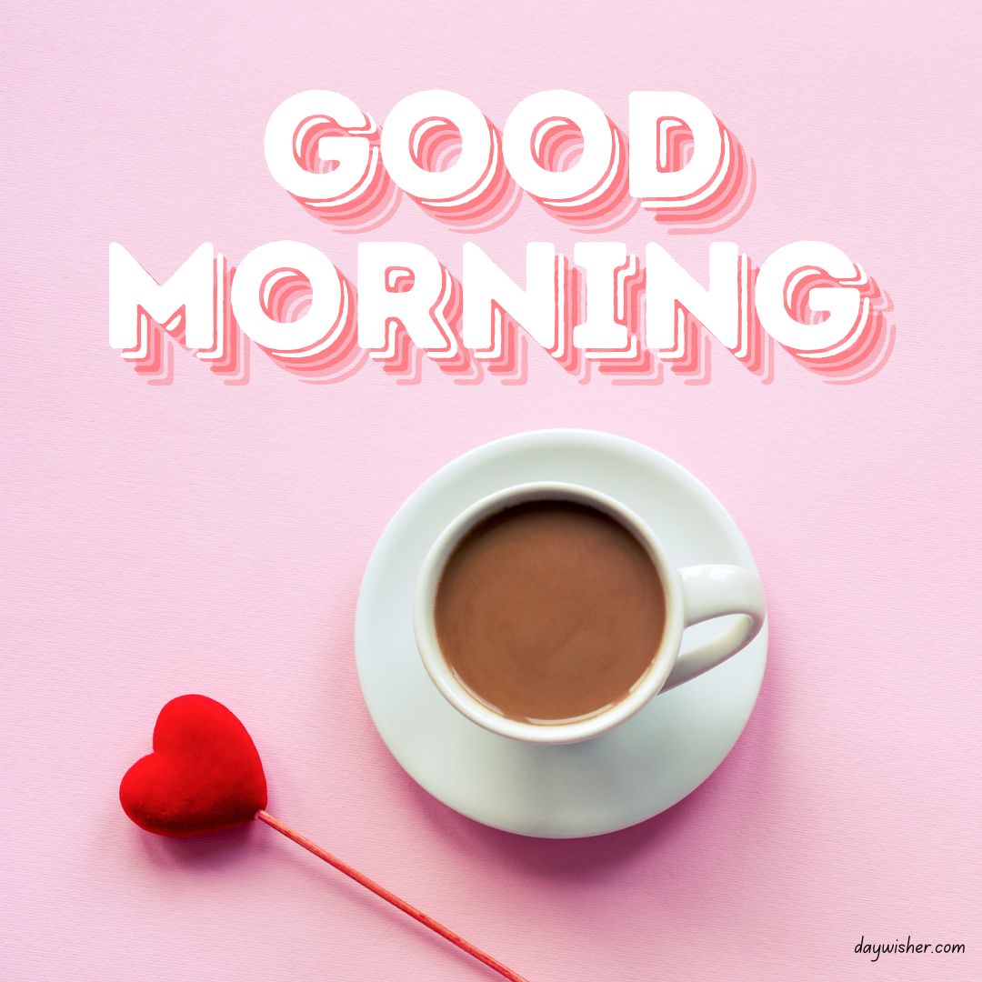 Uplift your spirits with this lovely good morning coffee image, showcasing a cup of rich coffee next to a plush red heart on a stick, all set against a soft pink background, creating a sweet and romantic ambiance for your morning.