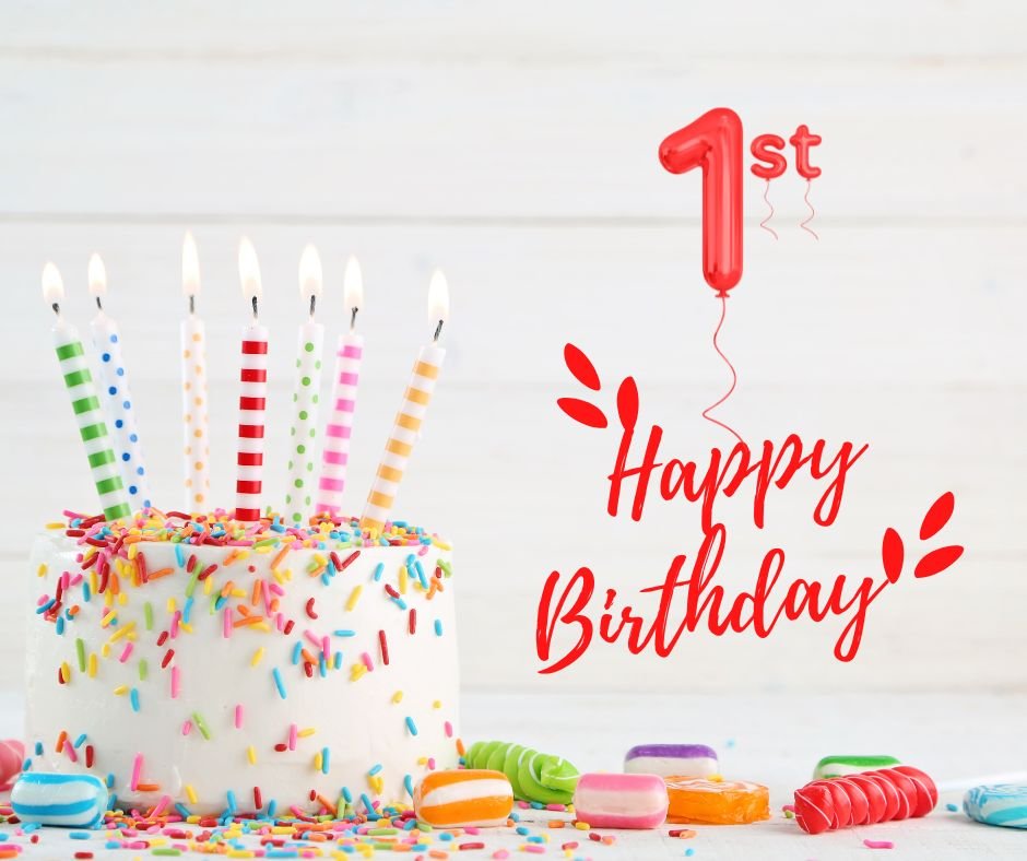 A colorful birthday celebration with a cake topped with lit candles, scattered candies, and a "Happy 1st Birthday" balloon against a wooden background.