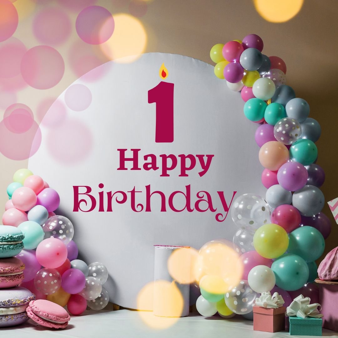A colorful first birthday party setup featuring a sign that reads "Happy 1st Birthday," surrounded by balloons, gifts, and macarons, with a bokeh effect in the background.